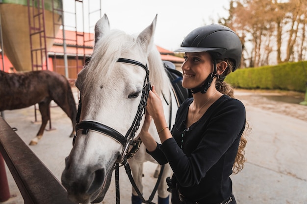 Jovem mulher caucasiana preparando um cavalo branco para um passeio