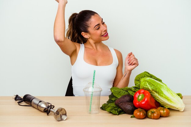 Foto jovem mulher caucasiana preparando um smoothie saudável com legumes, dançando e se divertindo.