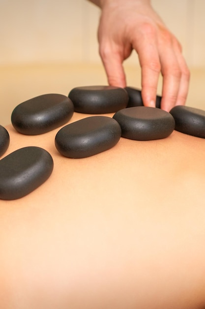 Jovem mulher caucasiana, recebendo massagem nas costas com pedras pretas por massagista em salão de spa. Uma mulher recebendo um tratamento de spa.