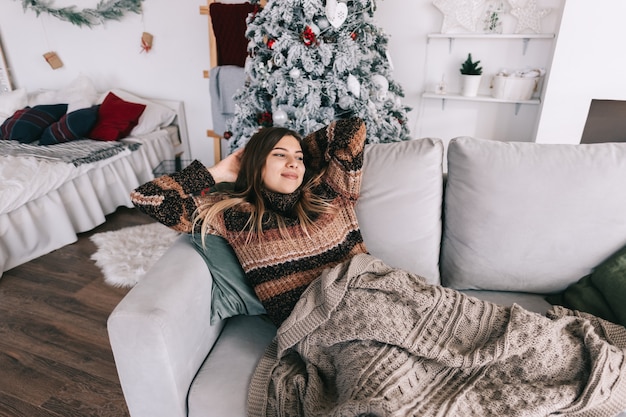 Jovem mulher caucasiana relaxando em um sofá em casa nas férias de Natal.