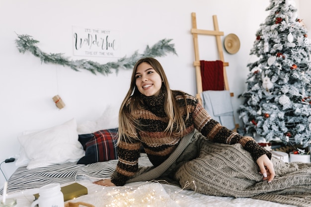 Jovem mulher caucasiana, relaxando em uma cama em casa nas férias de Natal.