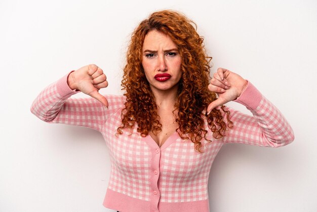 Foto jovem mulher caucasiana ruiva isolada no fundo branco, mostrando um gesto de desagrado polegares para baixo conceito de desacordo