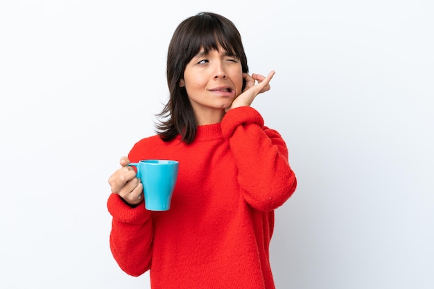 Jovem mulher caucasiana segurando a xícara de café isolada no fundo branco frustrada e cobrindo os ouvidos