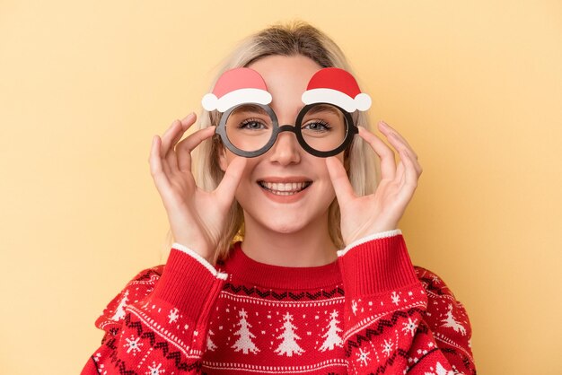 Jovem mulher caucasiana segurando adereços de natal isolados em fundo amarelo