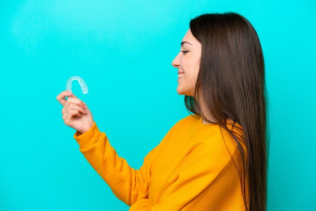 Jovem mulher caucasiana segurando aparelho invisível isolado em fundo azul com expressão feliz