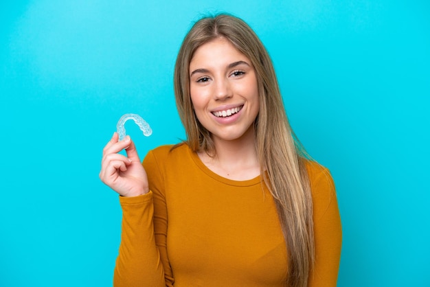 Jovem mulher caucasiana segurando aparelho invisível isolado em fundo azul sorrindo muito