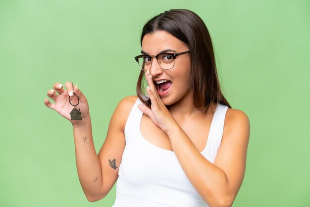 Foto jovem mulher caucasiana segurando as chaves de casa isoladas no fundo croma verde sussurrando algo