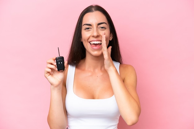 Jovem mulher caucasiana segurando as chaves do carro isoladas no fundo rosa gritando com a boca aberta