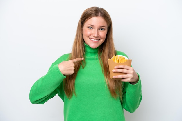 Jovem mulher caucasiana segurando batatas fritas isoladas no fundo branco com expressão facial de surpresa