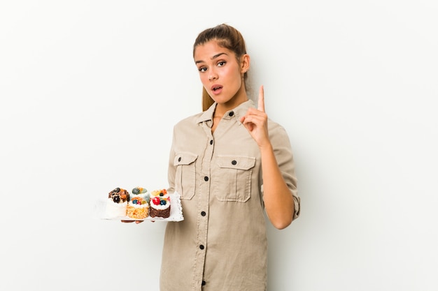 Jovem mulher caucasiana segurando bolos doces, tendo uma idéia, conceito de inspiração.