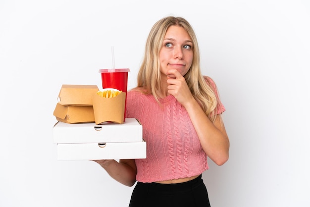 Jovem mulher caucasiana segurando comida gorda isolada em um fundo azul, tendo dúvidas e pensando