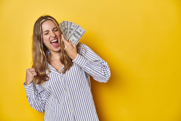 Foto jovem mulher caucasiana segurando dinheiro levantando o punho depois de um conceito vencedor da vitória