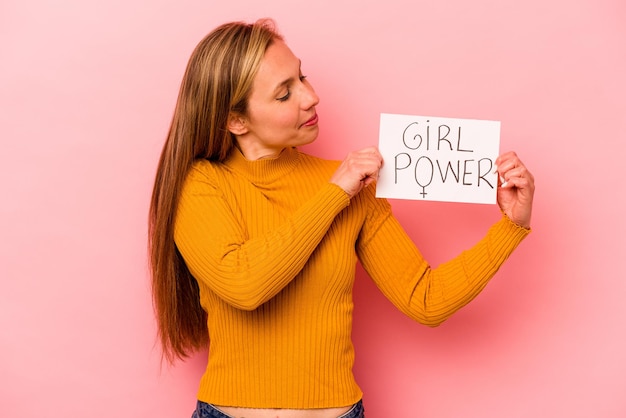 Jovem mulher caucasiana segurando o cartaz de poder feminino isolado no fundo rosa