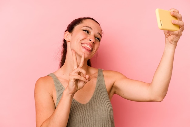 Jovem mulher caucasiana segurando o celular isolado no fundo rosa