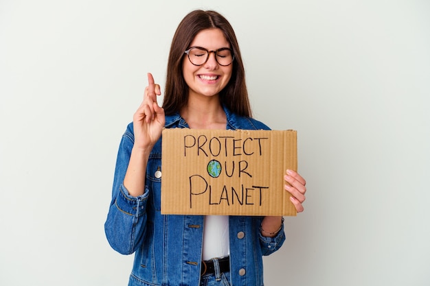 Jovem mulher caucasiana segurando proteger nosso cartaz de planeta isolado mostrando um espaço de cópia na palma da mão e segurando a outra mão na cintura.