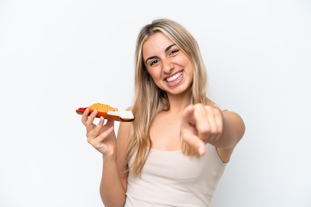 Jovem mulher caucasiana segurando sashimi isolado no fundo branco aponta o dedo para você com uma expressão confiante