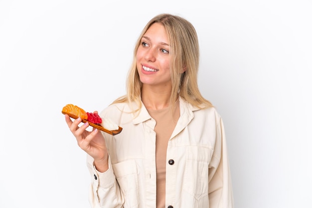 Jovem mulher caucasiana segurando sashimi isolado no fundo branco, olhando para o lado e sorrindo