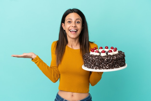 Foto jovem mulher caucasiana segurando um bolo de aniversário isolado em um fundo azul com expressão facial chocada