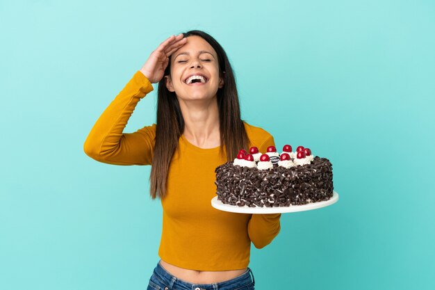 Jovem mulher caucasiana segurando um bolo de aniversário isolado em um fundo azul e sorrindo muito