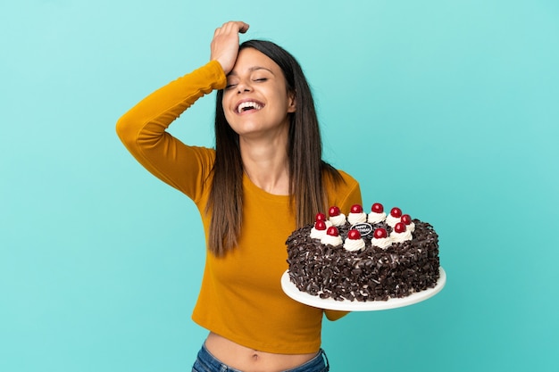 Jovem mulher caucasiana segurando um bolo de aniversário isolado em um fundo azul percebeu algo e tem a intenção de encontrar a solução