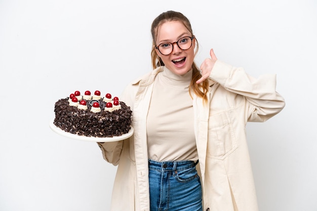 Jovem mulher caucasiana segurando um bolo de aniversário isolado no fundo branco fazendo gesto de telefone Ligue-me de volta sinal