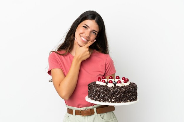 Jovem mulher caucasiana segurando um bolo de aniversário isolado no fundo branco, feliz e sorridente