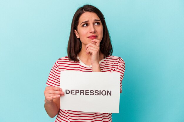 Jovem mulher caucasiana segurando um cartaz de depressão isolado em um fundo azul