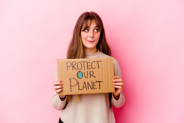 Jovem mulher caucasiana segurando um cartaz de proteger nosso planeta isolado confuso, sente-se em dúvida e inseguro.
