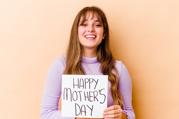 Jovem mulher caucasiana segurando um cartaz do dia das mães feliz isolada, rindo e se divertindo