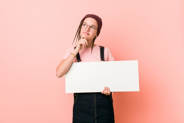 Jovem mulher caucasiana, segurando um cartaz, olhando de soslaio com expressão duvidosa e cética.