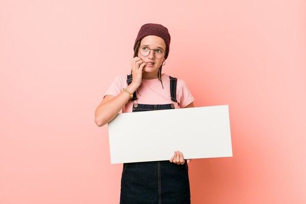 Jovem mulher caucasiana, segurando um cartaz, roer as unhas, nervoso e muito ansioso.