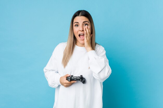 Jovem mulher caucasiana segurando um controlador de jogo gritando animado para a frente.