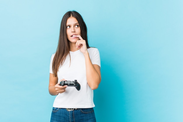 Jovem mulher caucasiana segurando um controlador de jogo relaxado pensando em algo olhando para um espaço de cópia.