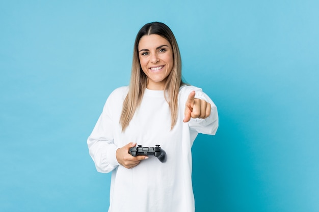 Jovem mulher caucasiana, segurando um controlador de jogo sorrisos alegres, apontando para a frente.