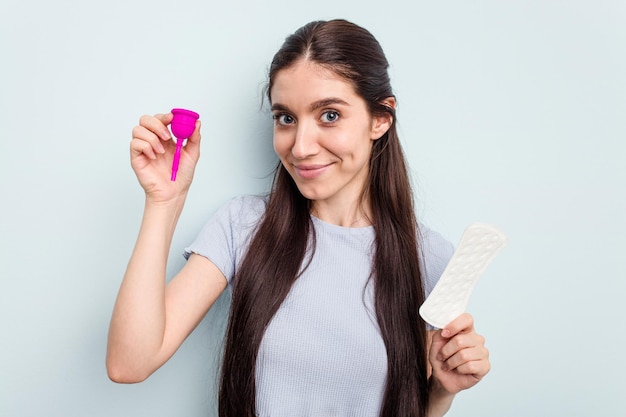 Jovem mulher caucasiana segurando um copo menstrual isolado em fundo azul