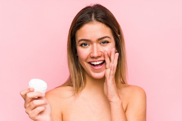 Jovem mulher caucasiana segurando um creme hidratante gritando animado para a frente.