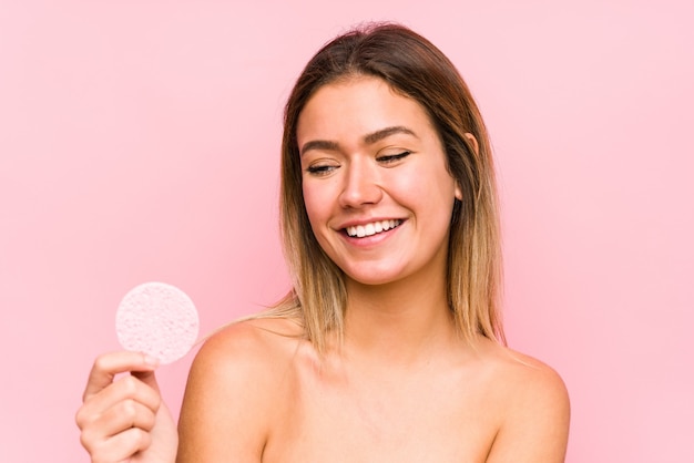 Jovem mulher caucasiana segurando um disco facial isolado, sorrindo confiante com os braços cruzados.