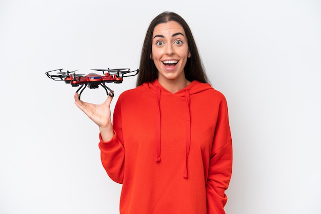 Jovem mulher caucasiana segurando um drone isolado no fundo branco com expressão facial de surpresa