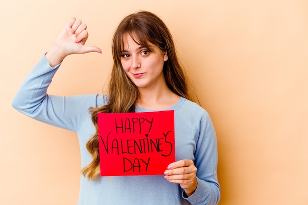 Jovem mulher caucasiana, segurando um feliz dia dos namorados isolado, sente-se orgulhosa e autoconfiante, exemplo a seguir.