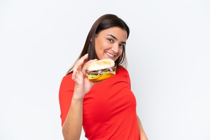 Foto jovem mulher caucasiana segurando um hambúrguer isolado em fundo branco com expressão feliz