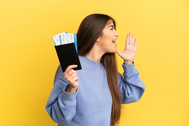 Jovem mulher caucasiana segurando um passaporte isolado em um fundo amarelo, gritando com a boca bem aberta para o lado