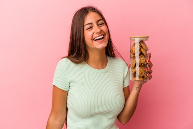 Jovem mulher caucasiana, segurando um pote de biscoitos isolado no fundo rosa, rindo e se divertindo.