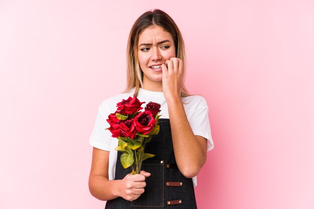 Jovem mulher caucasiana segurando um rosas isolado roer as unhas, nervosa e muito ansiosa.