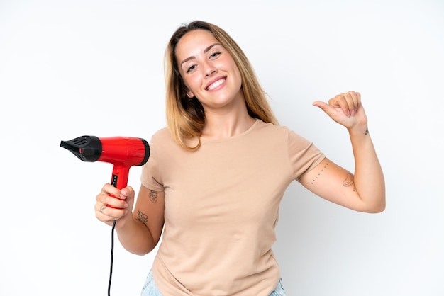 Jovem mulher caucasiana segurando um secador de cabelo isolado no fundo branco orgulhoso e satisfeito