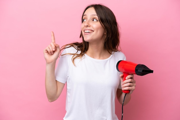 Jovem mulher caucasiana segurando um secador de cabelo isolado no fundo rosa com a intenção de perceber a solução enquanto levanta um dedo