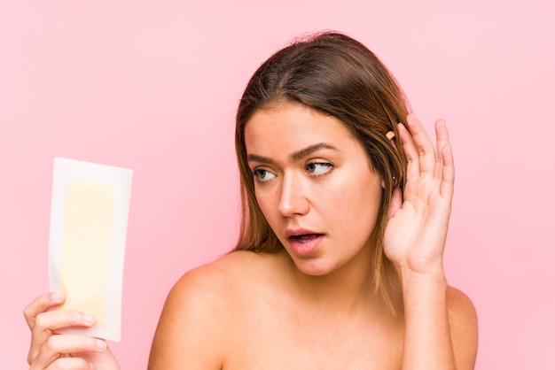 Jovem mulher caucasiana, segurando uma banda depilatória isolada tentando ouvir uma fofoca.