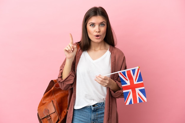 Jovem mulher caucasiana segurando uma bandeira do Reino Unido isolada em um fundo rosa com a intenção de descobrir a solução enquanto levanta um dedo