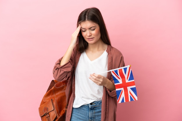 Jovem mulher caucasiana segurando uma bandeira do Reino Unido isolada em um fundo rosa com dor de cabeça