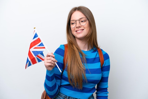 Jovem mulher caucasiana segurando uma bandeira do Reino Unido, isolada no fundo branco, olhando para o lado e sorrindo