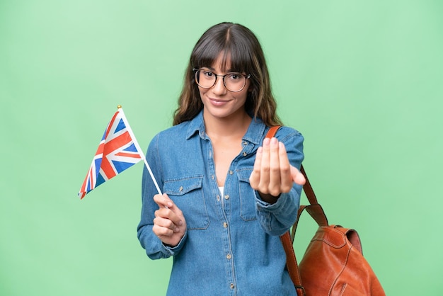 Jovem mulher caucasiana segurando uma bandeira do Reino Unido sobre fundo isolado convidando para vir com a mão feliz que você veio